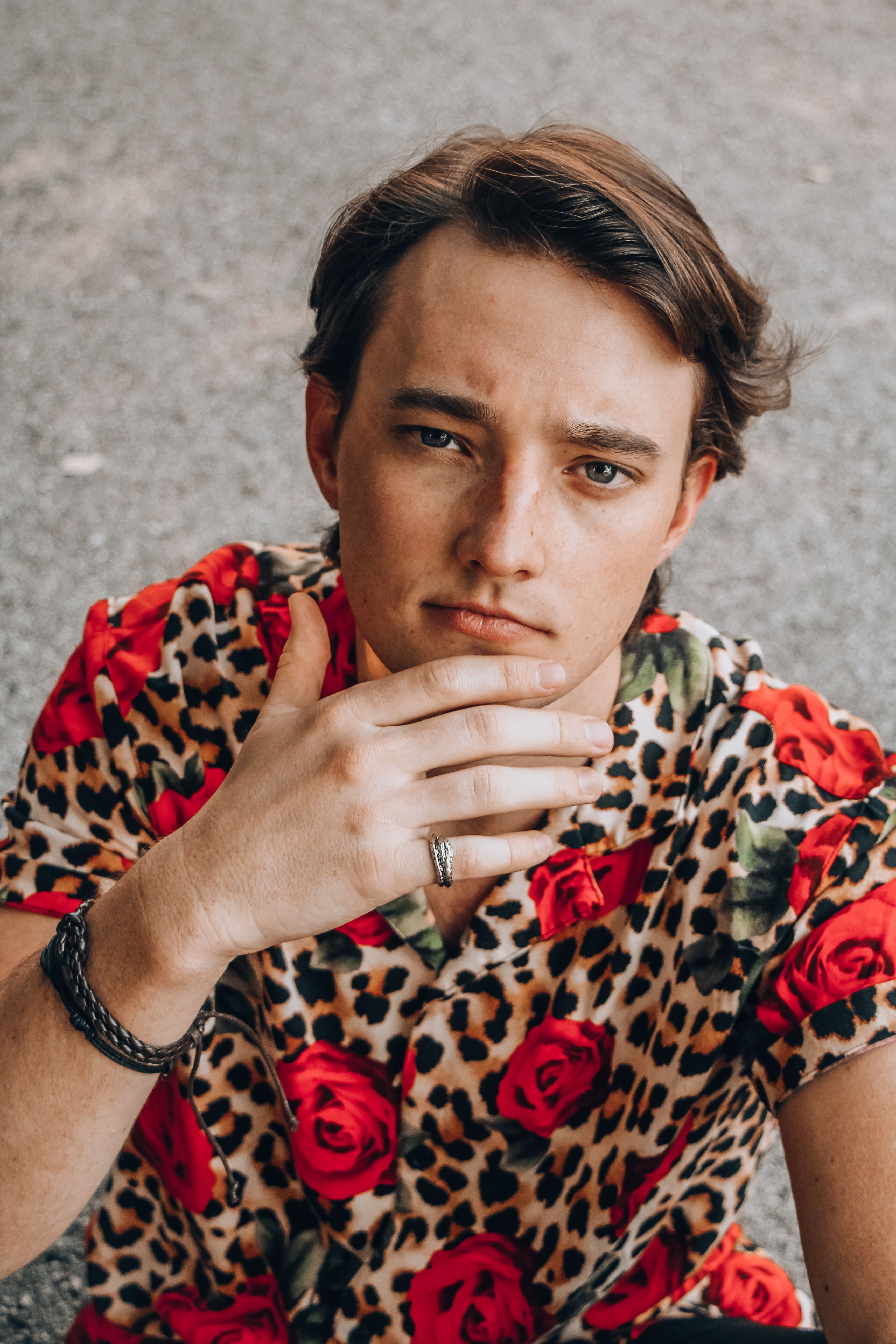 From above of young pensive male in leopard clothes touching chin on roadway and looking at camera