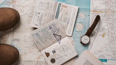 Flat lay of travel essentials featuring a map, camera, and passport stamps, perfect for wanderlust inspiration.
