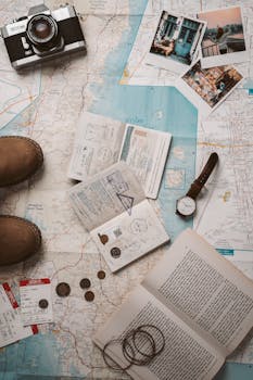 Flat lay of travel essentials featuring a map, camera, and passport stamps, perfect for wanderlust inspiration.
