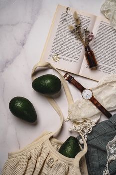 Creative flat lay with avocados, wristwatch, and open book on a marble surface.