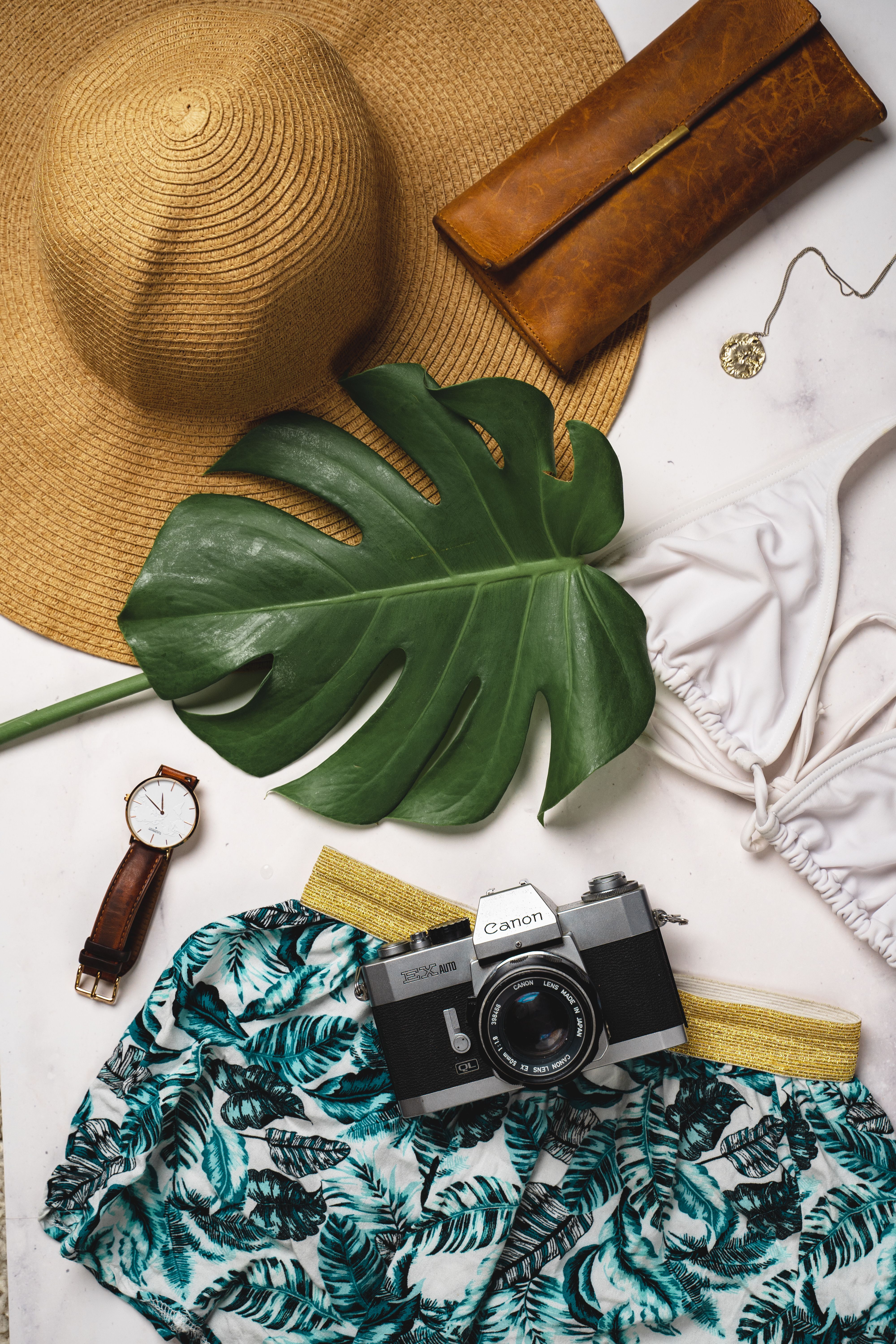 A flat lay of beach essentials including a straw hat, swimsuit, and vintage camera.. flat, beach, essentials