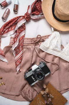 A creative flat lay of summer essentials featuring a vintage camera, patterned scarf, and accessories.