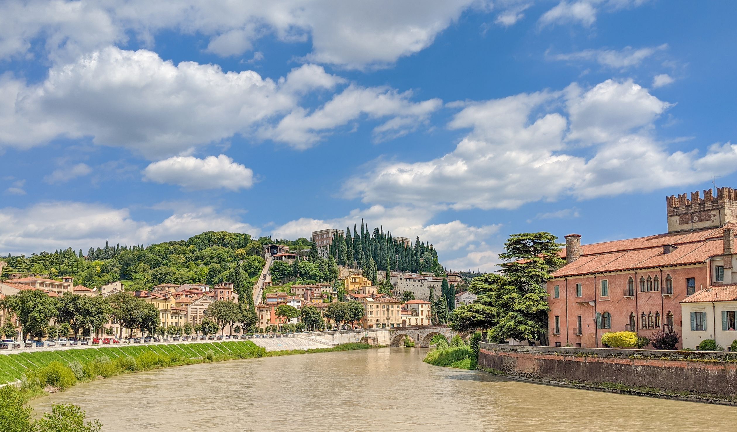 Picturesque view of Verona with the Adige river, lush hills, and historic architecture.