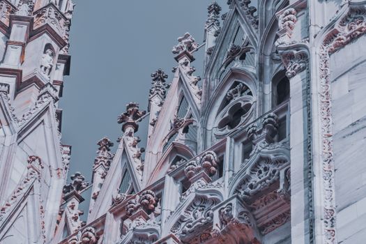 From below exterior details of Milan Cathedral with ornamental elements and sculptures under gray sky