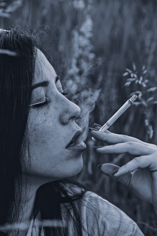 Thoughtful young woman smoking cigarette in nature