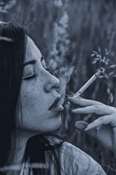 一位年轻女子在大自然的环绕下，于户外吸烟的肖像