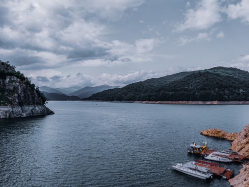 Free Rocky mountains covered with trees with lush foliage near vast rippling water of lake with pier Stock Photo