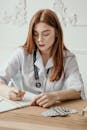年轻的女医生在办公桌上写笔记，桌上放着听诊器和药物