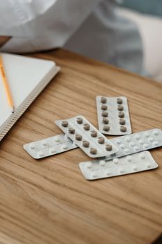 在木制表面上选择药丸和带铅笔的笔记本，以突出医疗保健主题