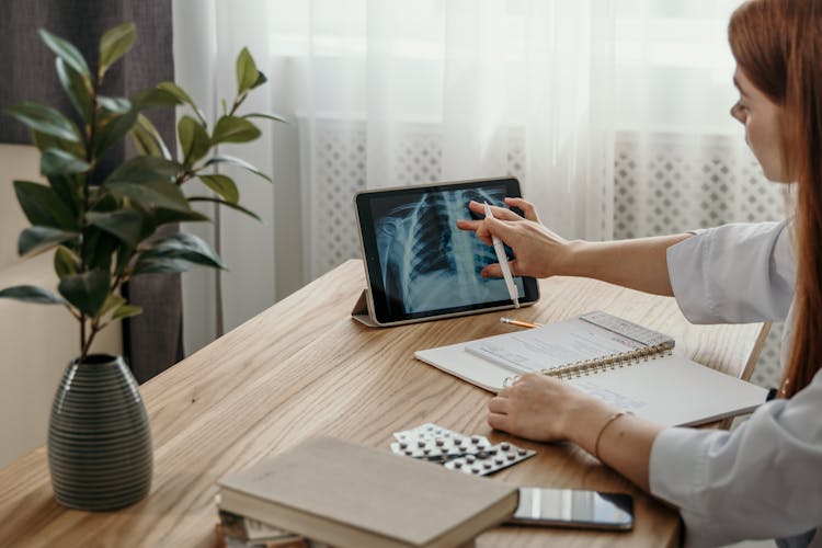 A Woman In White Long Sleeves Looking At The Image On The Tablet