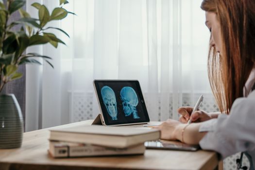 Doctor in office reviewing skull X-ray on tablet, taking notes for diagnosis.