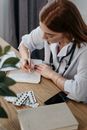 年轻的女医生在附近放着听诊器和药丸的医疗办公室里开处方