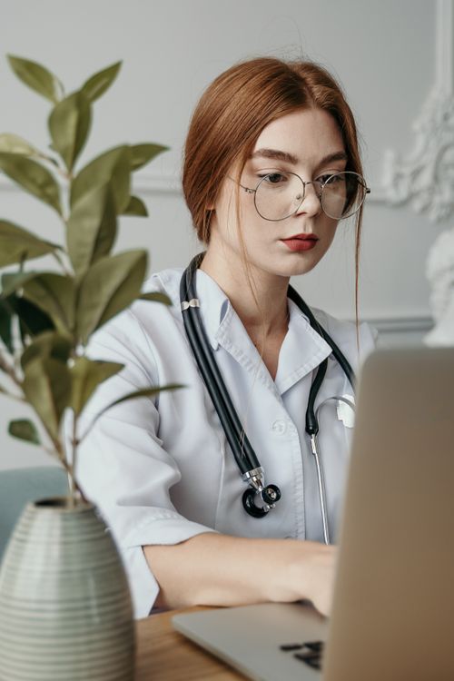 Free Portrait of a female doctor in medical scrubs with a stethoscope, focused on her laptop. Stock Photo
