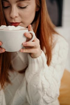 一位女士穿着舒适的针织毛衣，正享受着棉花糖热巧克力