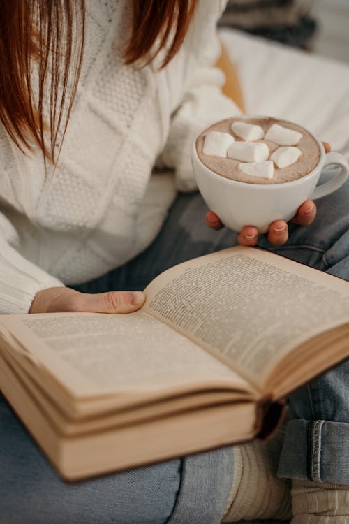 Close Up Photo of Person Holding Book and a Cup