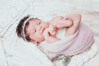 毯子里包裹着可爱的新生婴儿，柔软的床上用品上放着花卉头带