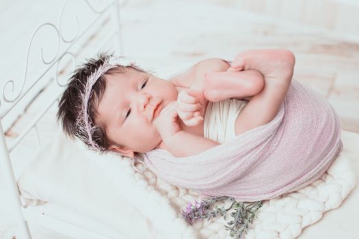 毯子里包裹着可爱的新生婴儿，柔软的床上用品上放着花卉头带