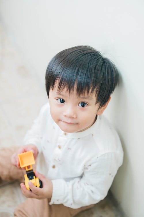 Free Boy Sitting on the Floor While Holding a Toy Stock Photo