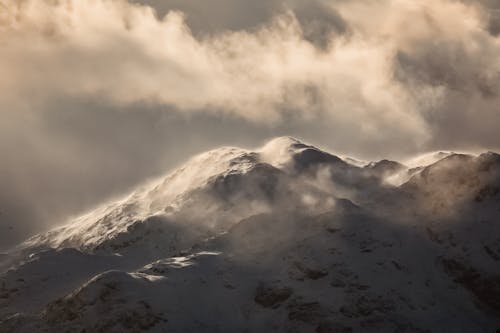 Free Splendid scenery of snowy mountain range in evening sunlight against gray cloudy sky Stock Photo