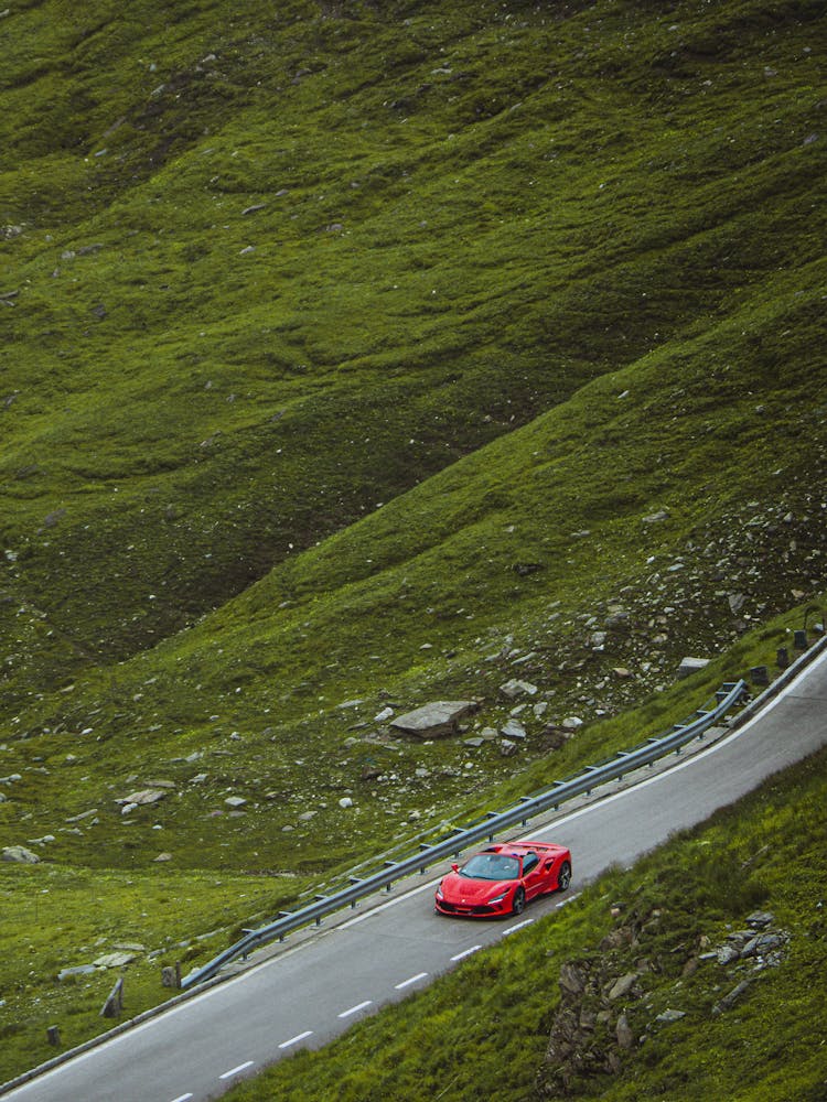 Red Sports Car Driving On Road In Green Valley