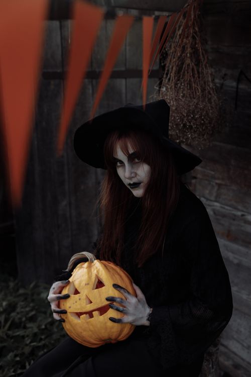 Free Eerie witch in a dark costume holds a carved pumpkin, perfect for Halloween ambiance. Stock Photo