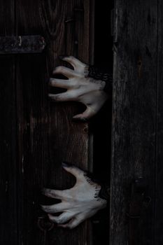 一只长着黑色指甲的怪异白手穿过深色木门，非常适合万圣节主题