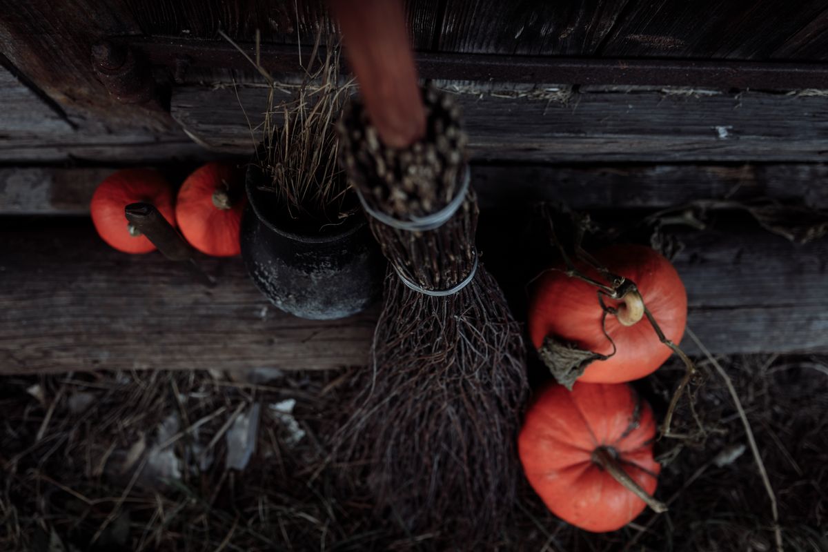 A witch's broom and pumpkins against a rustic wooden backdrop