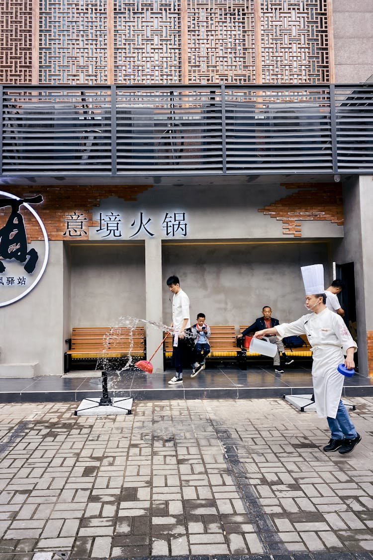 Man In White Chef Uniform Throwing Water On Pavement