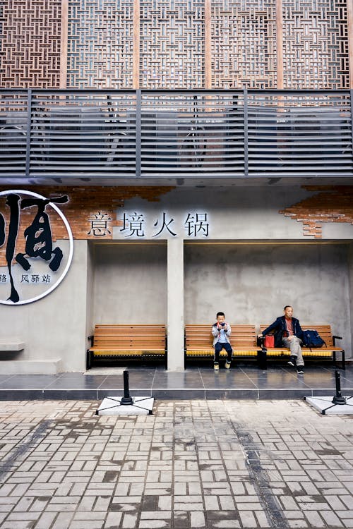 Man and Boy Sitting on Benches by Building