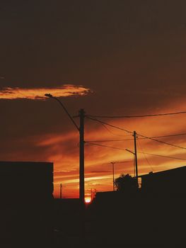 Silhouette of city buildings and electric poles against a vibrant sunset sky.