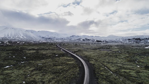 Aerial view of a winding road through Iceland's snow-capped mountains and open fields during winter.