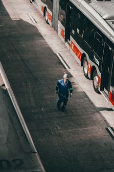 From above of unrecognizable male engineer with metal line in hand in uniform and protective helmet walking on asphalt road near parked modern bus