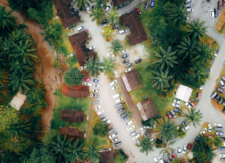 Drone view of automobiles parked near accommodation houses surrounded by green palms in tropical country