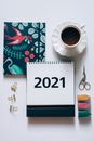 办公桌的顶视图里，放着一杯咖啡、一本2021年日历、一个彩色笔记本和一些文具