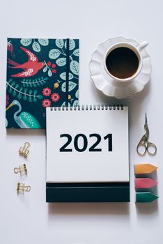 办公桌的顶视图里，放着一杯咖啡、一本2021年日历、一个彩色笔记本和一些文具
