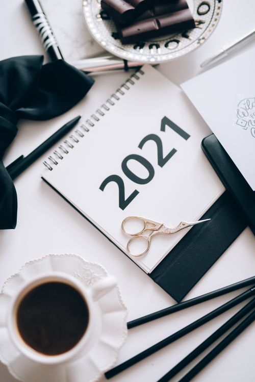 Free Flatlay of a 2021 planner with coffee, scissors, and decorative items on a desk. Stock Photo