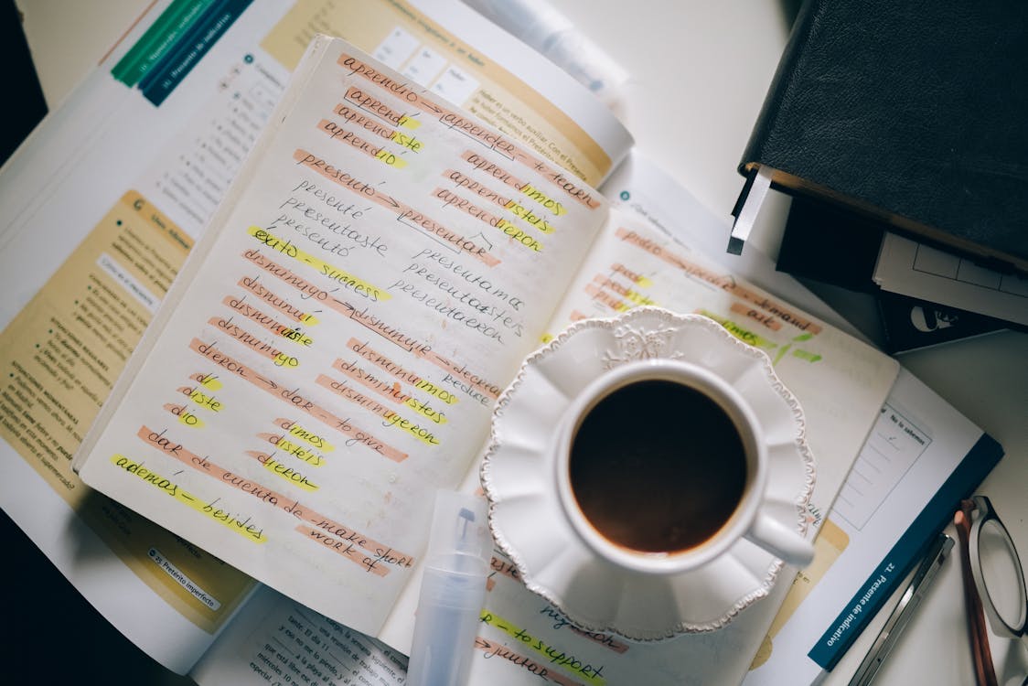 Free A Cup of Black Coffee on a Notebook with Notes of Foreign Language with Translation Stock Photo