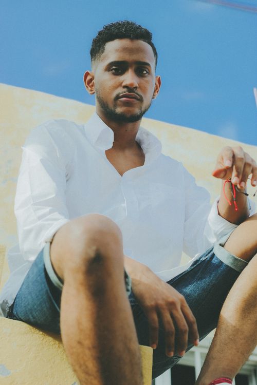 Free A fashionable man in a white shirt and denim shorts posing outdoors on a sunny day. Stock Photo