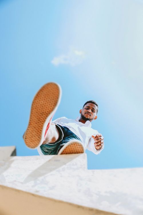 Free Low-angle shot of a man outdoors against a blue sky, emphasizing footwear. Stock Photo
