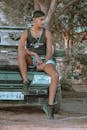 Man in Black Tank Top Sitting on Car Hood