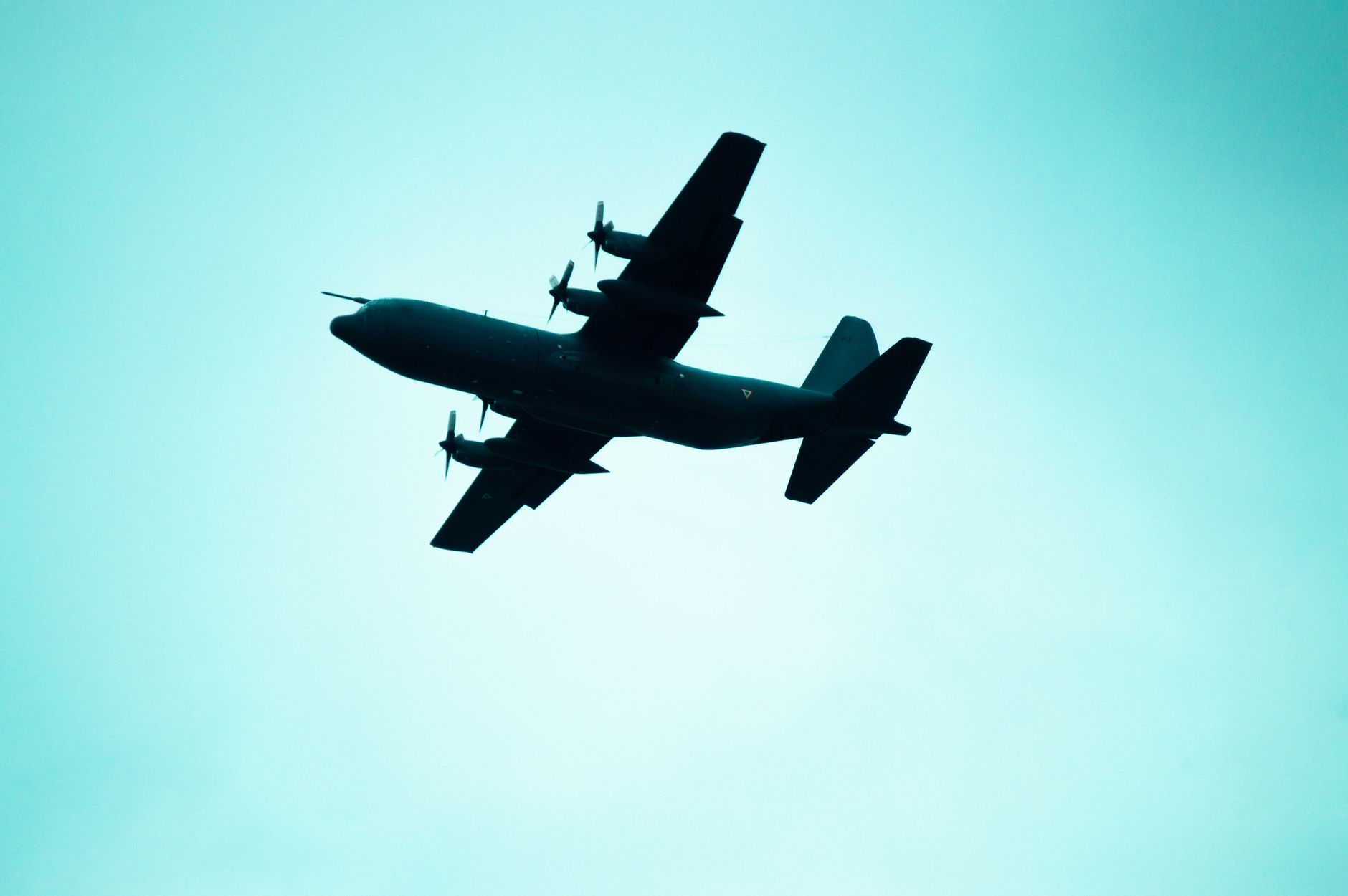 A silhouette of a military plane flying in a clear, blue sky, highlighting its aerodynamic design.