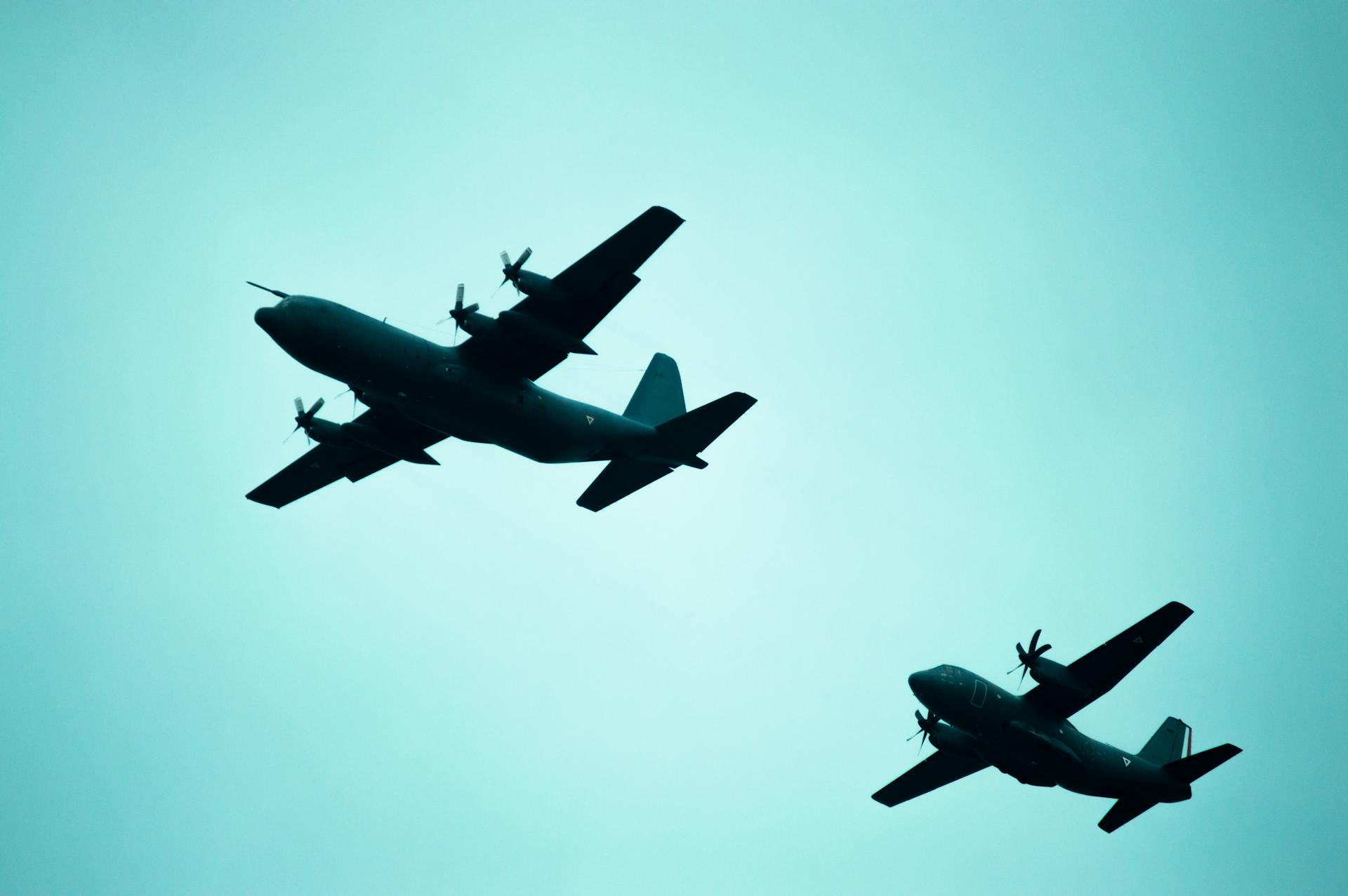 Silhouetted military aircrafts flying in formation against a clear sky.