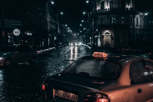 A rainy night city street scene with a parked taxi and reflections on wet cobblestones.