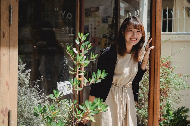 Smiling Asian woman in apron standing on store doorway
