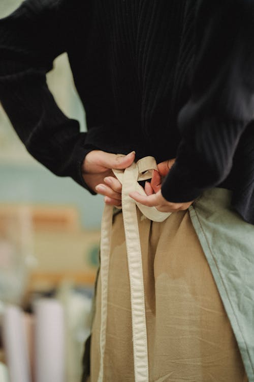 Back view crop anonymous female cafeteria or store worker tying up apron lace straps before duty