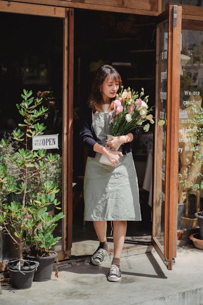 Positiver Asiatischer Weiblicher Floristería, Der Mit Blumenstrauß An Der Ladentür Steht · Kostenloses Stock-Foto