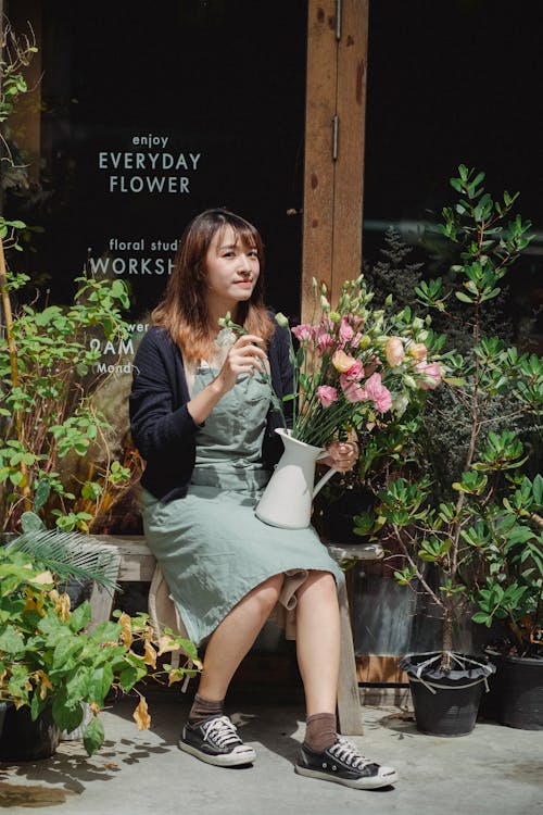 Content Asian female florist sitting on bench with bouquet