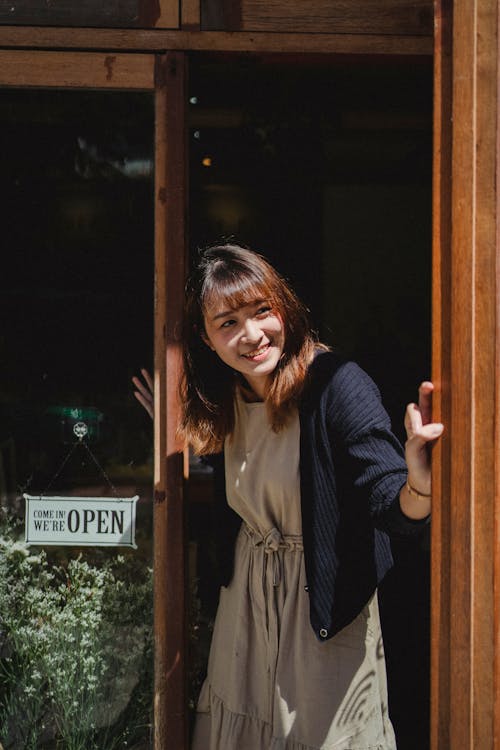 Free Positive smiling Asian female store worker opening store door and looking away contentedly Stock Photo