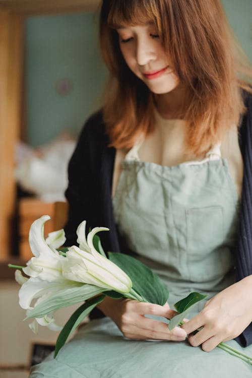 Crop serene Asian female florist sitting with white lily flower