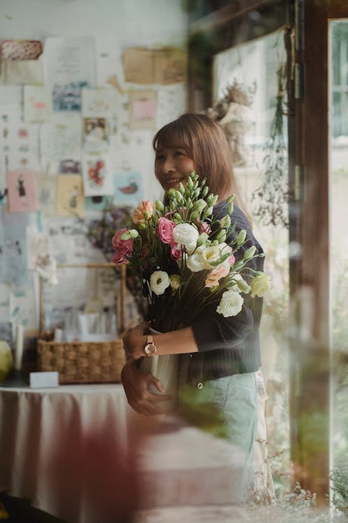 Cheerful ethnic woman standing with bouquet of flowers